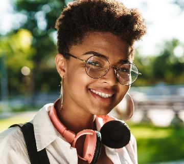Smiling person with headphones and glasses outdoors.