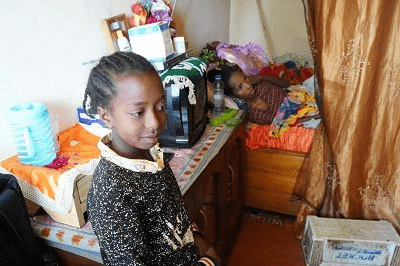 Child standing in a cozy, cluttered room.