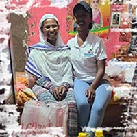 Two women sitting on a bed, smiling.