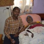 Man sitting beside person in hospital bed.