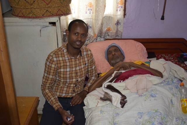Man sitting beside person in hospital bed.